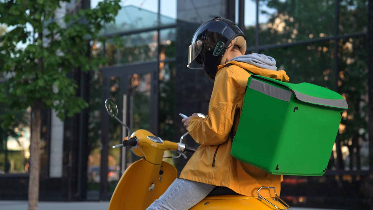 Livreur assis sur un scooter à l'arrêt, consultant son smartphone